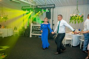 Party guests dancing in a line formation under yellow and blue lighting at an indoor event.