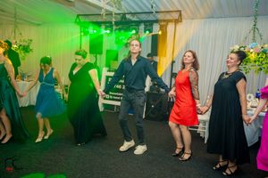 Wedding celebration with green lighting effects and guests dancing in formal wear.
