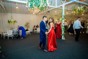 Wedding guests dancing in a spacious white reception hall with hanging greenery decorations.