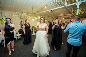 Wedding reception guests dancing together on a dance floor decorated with greenery and white decor.