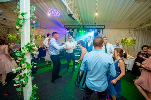 Wedding reception venue with green uplighting and floral decorations along white pillars.