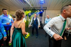 Wedding party dancing and celebrating under green and blue lighting at an indoor reception.