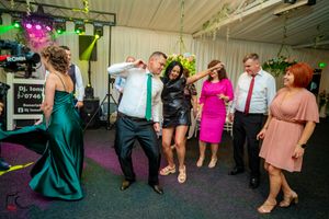 Wedding celebration with guests dancing under multicolored lighting in a decorated indoor space.