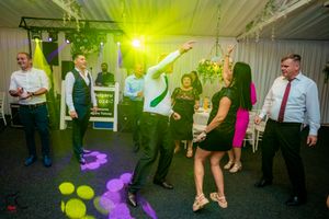 Wedding reception dance floor with colorful green lighting and guests dancing in a decorated indoor venue.