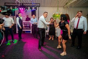 Wedding guests dancing under colorful lighting in a tented reception space.