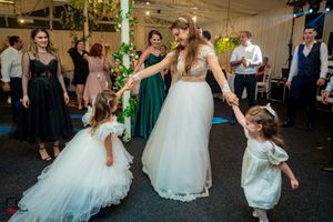 Bride in white gown dancing with flower girls at wedding reception.