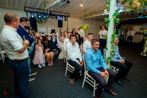 Wedding venue with exposed ceiling beams decorated with green lighting and hanging greenery.