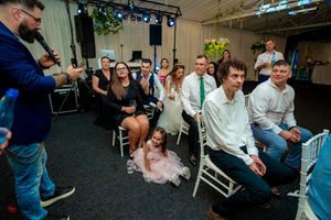 Indoor event space with guests seated in chairs under decorative green lighting and floral accents.