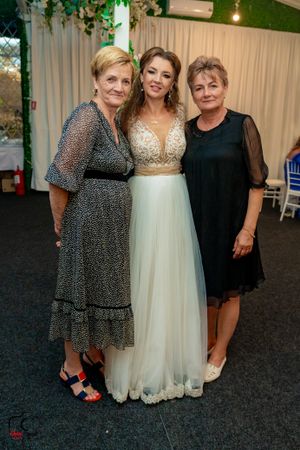 Wedding celebration showing guests in elegant dresses posing together at an indoor reception venue.
