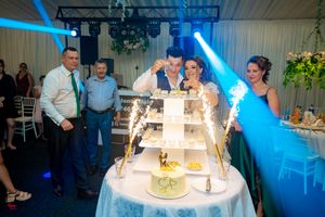 Reception hall bathed in blue lighting with guests gathered around wedding cake display.