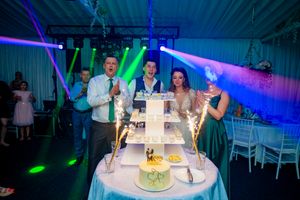 Elegant wedding reception setup with tiered cake display under purple and blue theatrical lighting.