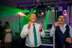 Wedding guests hold sparklers while celebrating with dramatic green and purple lighting effects.