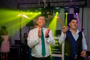 Party guests enjoying sparklers during wedding reception with colorful stage lighting effects.