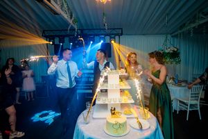 Wedding party celebrates around illuminated cake tower with dramatic blue lighting and sparkler effects.
