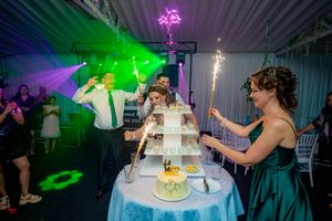 Celebratory moment at wedding reception with sparklers and colorful lighting around multi-tiered cake display.