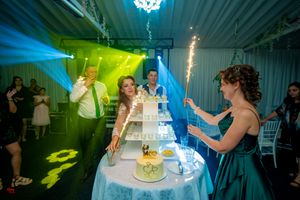 Wedding party celebrates around a tiered cake display illuminated by dramatic blue and green lighting at a reception.