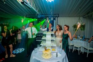 Wedding party celebrates beside a tiered cake display with dramatic turquoise lighting effects.
