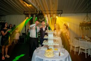 Wedding cake ceremony captured under warm yellow venue lighting.