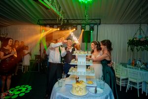 Wedding celebration with tiered cake illuminated by green spotlights in reception venue.