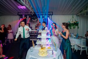 Multi-tiered wedding cake displayed at reception with dramatic purple and blue lighting effects.