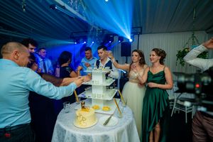 Wedding reception features dramatic blue uplighting as guests celebrate around a tiered cake.