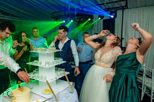 Wedding party celebrates near a white tiered cake under dramatic green and blue lighting effects.