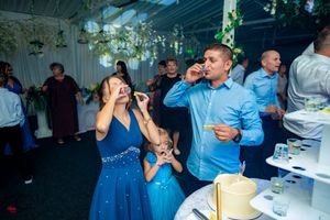 Party guests in blue and formal attire mingling at an event with decorative lighting.