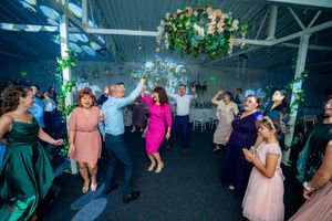 Wedding celebration with guests dancing under green and pink lighting with floral decorations.
