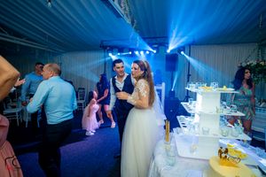 Wedding reception scene near white tiered cake with blue ambient lighting.
