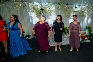 Wedding guests line the walls of a decorated reception venue with hanging greenery and lights.
