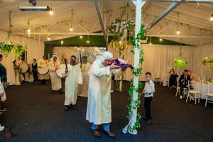 Guests dancing and celebrating at an indoor wedding reception with overhead lighting and decorative elements.
