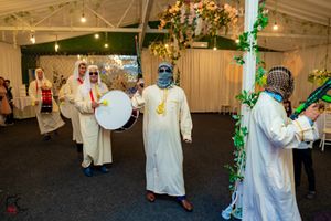 Wedding guests in white robes dance and celebrate during a festive reception under string lights and greenery.