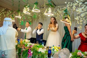 Wedding celebration with guests reacting joyfully under decorative hanging flowers and greenery.