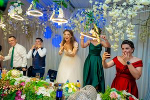 Wedding party celebrates at decorated reception table with hanging floral arrangements and blue lighting.