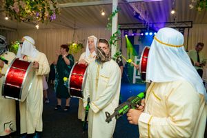 Musicians in traditional Middle Eastern attire perform with drums at an evening celebration.