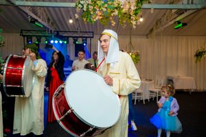 Traditional performers in white robes play large drums at an indoor wedding celebration.