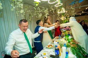 Wedding party toasting across a banquet table decorated with greenery and ambient lighting.