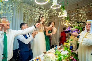 Wedding guests raise glasses in celebration at a festively decorated reception with hanging floral arrangements.