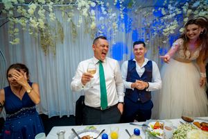 Lively wedding reception scene with guests laughing and celebrating at decorated table.