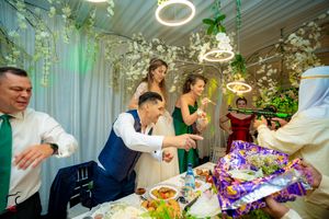 Wedding reception party with guests gathered around decorated table under circular lighting fixtures.