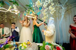 Festive wedding reception scene with guests dancing and celebrating under decorative lighting.