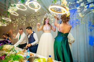 Wedding party celebrating at decorated reception table with overhead ring lights and floral decor.