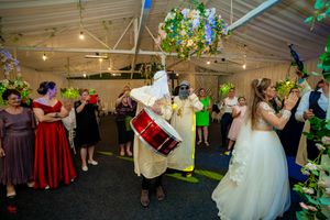 Wedding reception dance party with guests in formal attire under decorative lighting and greenery.
