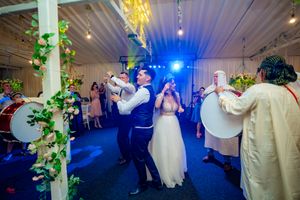 Festive wedding party dancing under blue lights and decorative greenery in an indoor reception space.