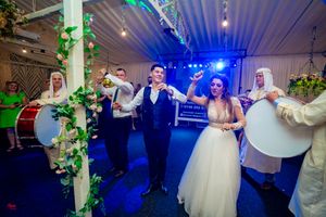 Wedding reception features lively dancing and celebrations under blue mood lighting and floral decor.