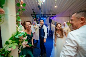 Wedding celebration with guests dancing on blue-lit dance floor surrounded by floral decorations.