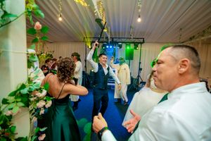 Wedding guests dancing and celebrating near decorative floral arrangements in reception venue.