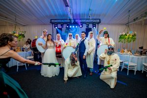 Wedding group photo in reception venue with dramatic blue lighting and table settings visible.