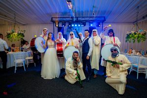 Wedding celebration group shot with guests wearing traditional robes and formal attire under blue lighting.
