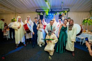 Wedding party in mix of traditional Middle Eastern attire and formal wear posing under stage lights.